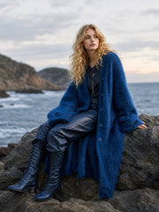 Gilet long ample boutonné bleu marine — vue portée en pied, assise sur des rochers au bord de la mer