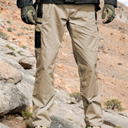 Pantalon tactique poches zippées kaki — vue portée de face, paysage rocheux