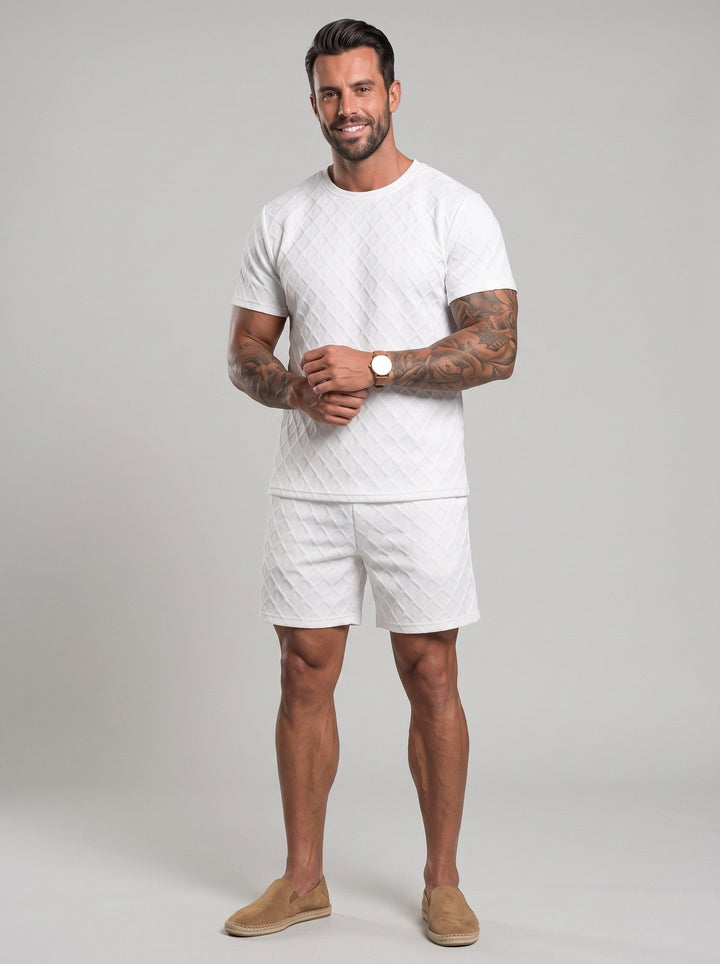 Homme debout en studio portant un ensemble blanc composé d’un t-shirt et d’un short à motif de losanges.