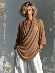 Pull camel col drapé asymétrique — vue portée en pied, pantalon blanc large, une main dans la poche
