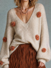 Pull beige avoine pompons orange — gros plan de l'encolure en V et des fleurs orange appliquées