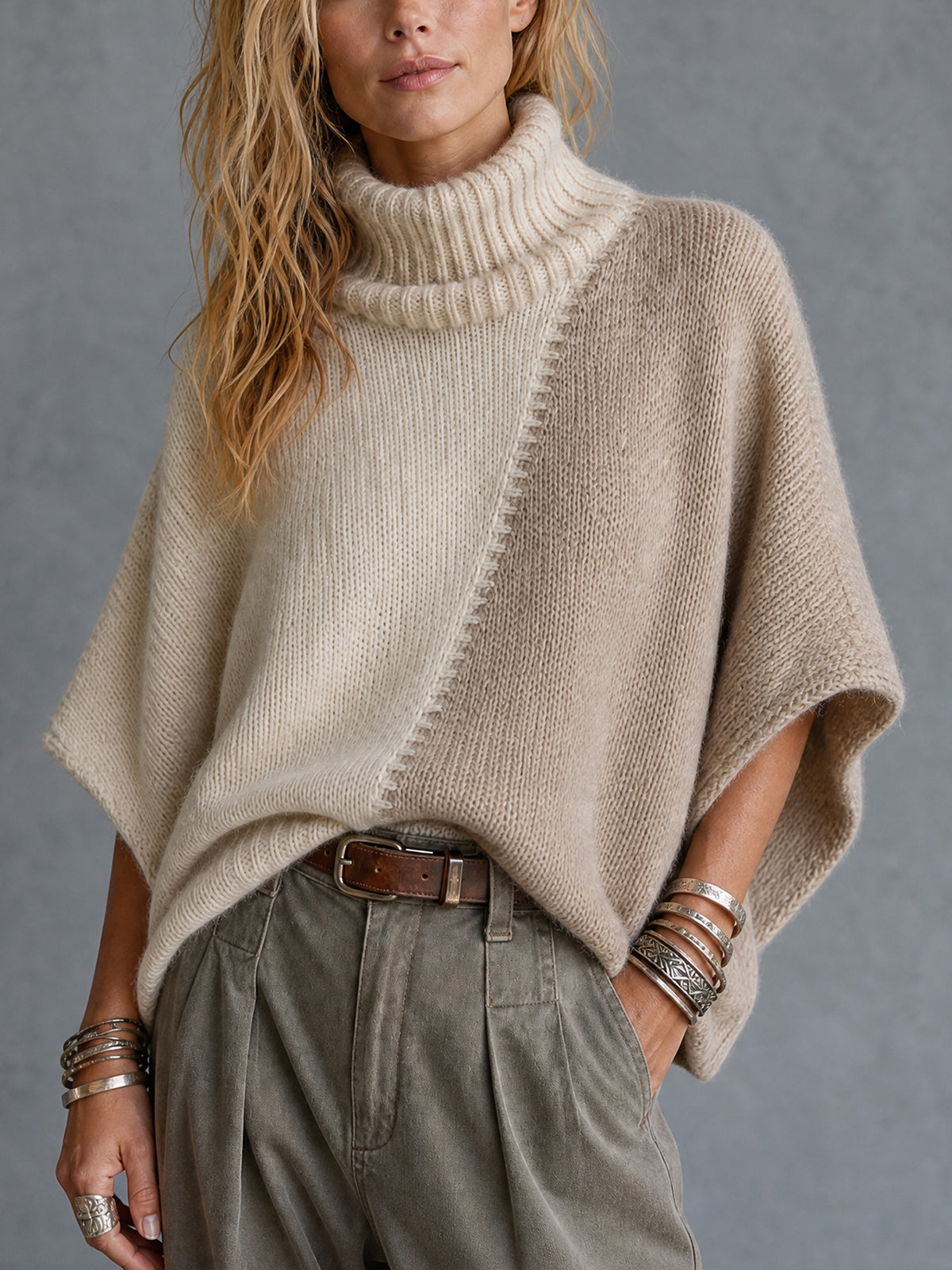 Poncho crème taupe col montant — vue portée de face, mains dans les poches d'un pantalon vert olive
