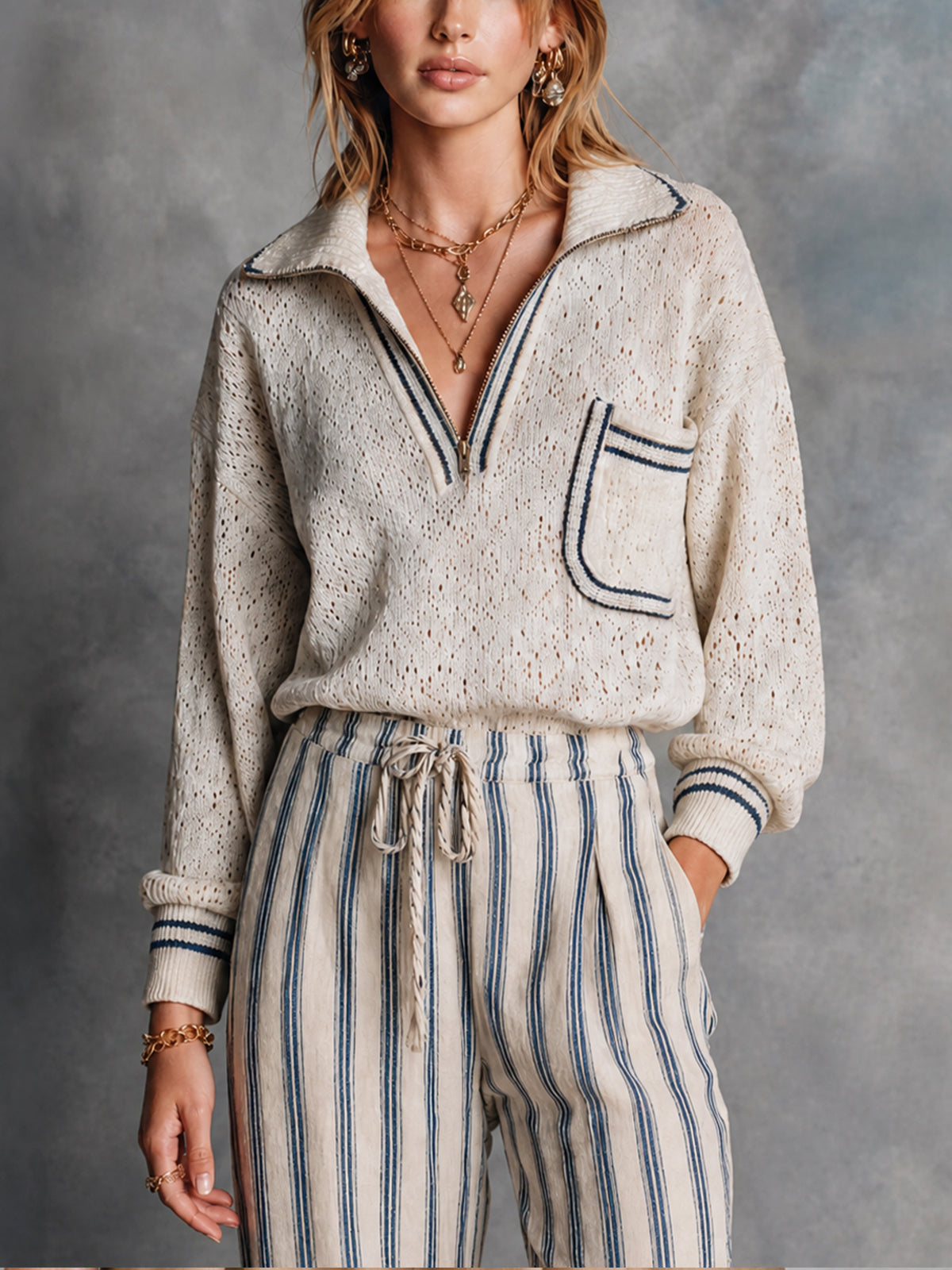 Pull crème marine zippé — vue portée de face, col pointu et poche poitrine à liseré foncé, pantalon rayé