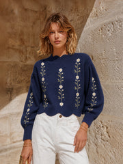 Pull bleu marine à fleurs — vue portée en pied, mains dans les poches d'un pantalon blanc