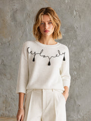 Pull écru motif manuscrit — vue portée en pied, mains dans les poches