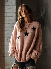 Pull rose à motifs étoiles — vue portée de face, plan plus large devant un mur en briques clair