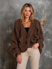 Cardigan brun à torsades — vue portée de face, une main dans la poche du pantalon