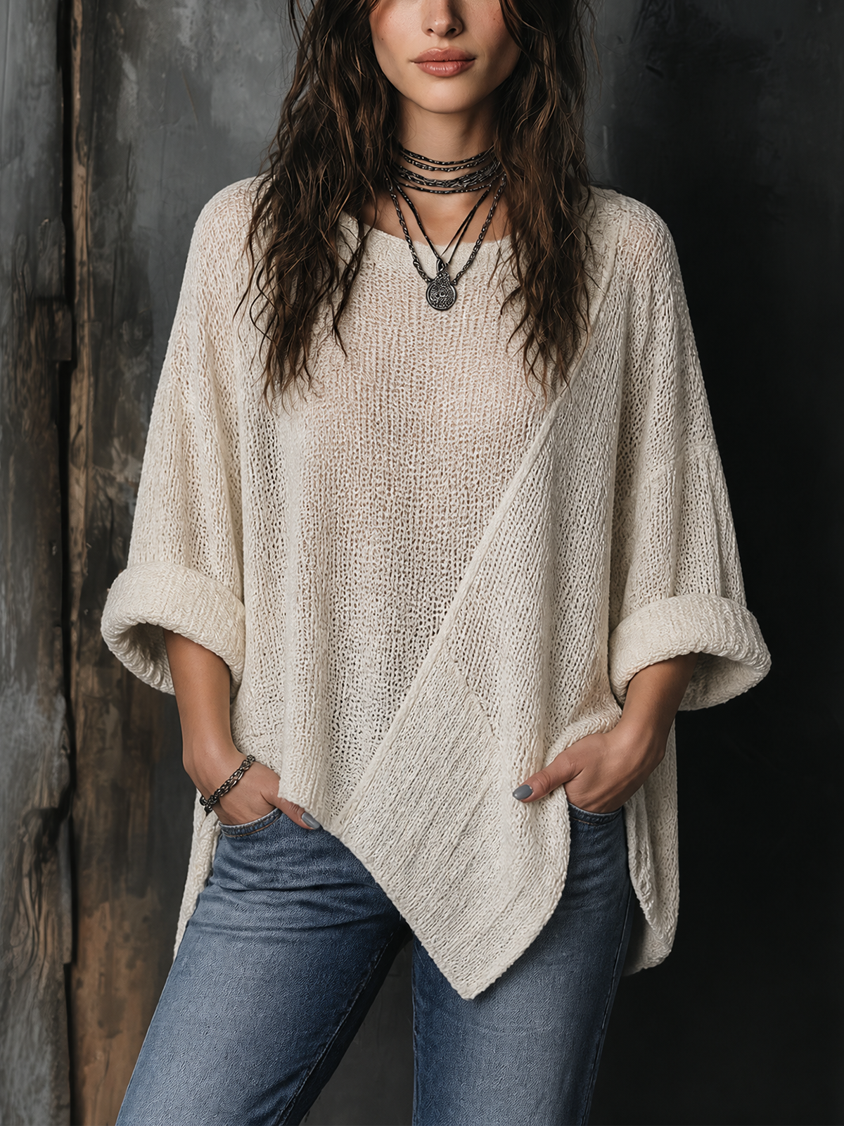 Pull blanc cassé ourlet asymétrique — vue portée de face, devant un mur sombre, jean bleu et collier noir
