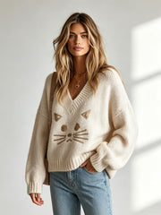 Pull beige chat col V — vue portée de trois-quarts, près d'une fenêtre lumineuse