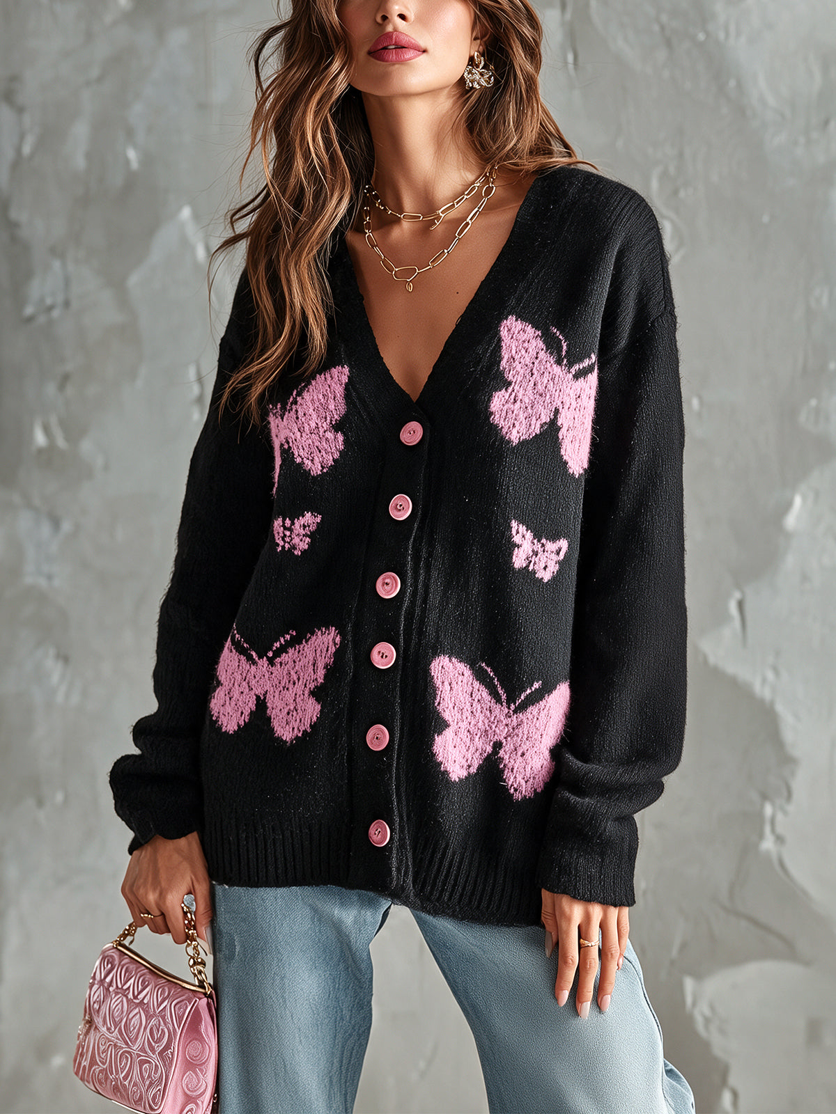 Cardigan noir rose à papillons — vue portée de face, petit sac rose et jean bleu, devant un mur gris