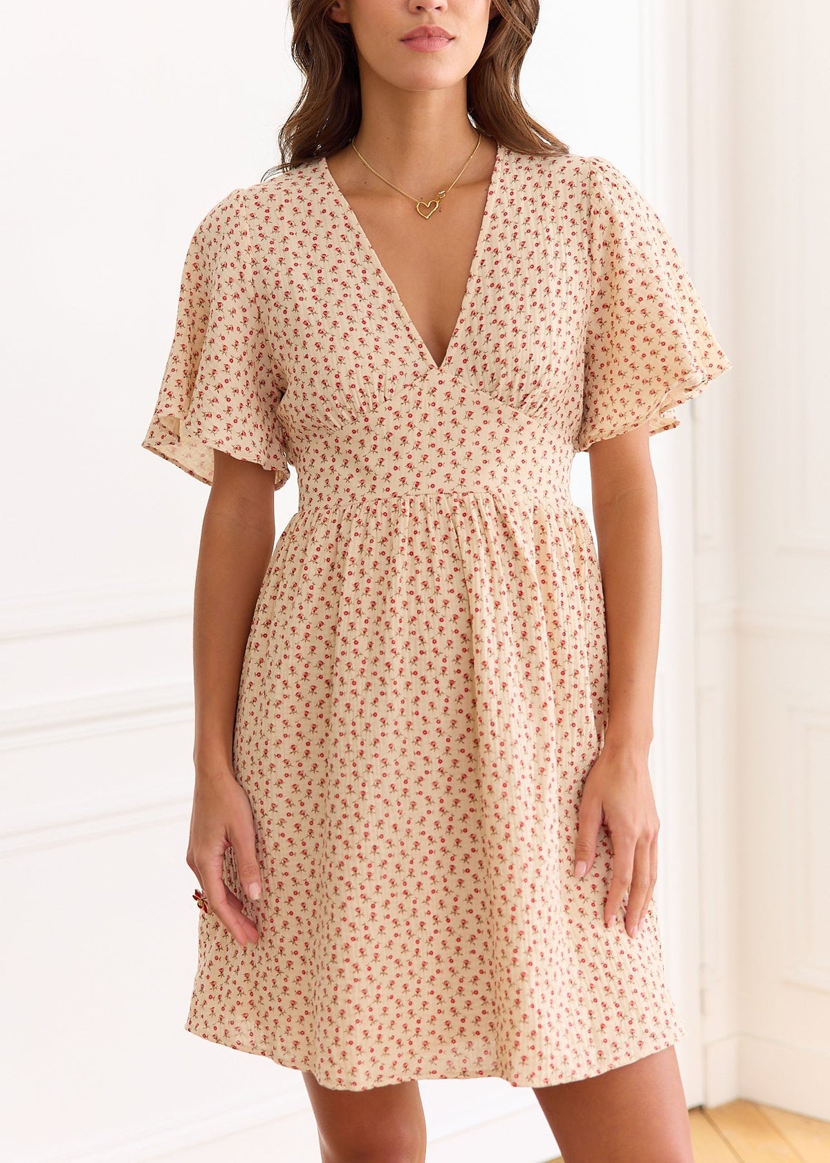 Robe courte beige à petites fleurs rouges, manches courtes et décolleté en V, portée de face.