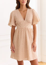 Robe courte beige à petites fleurs rouges, manches courtes et décolleté en V, portée de face.