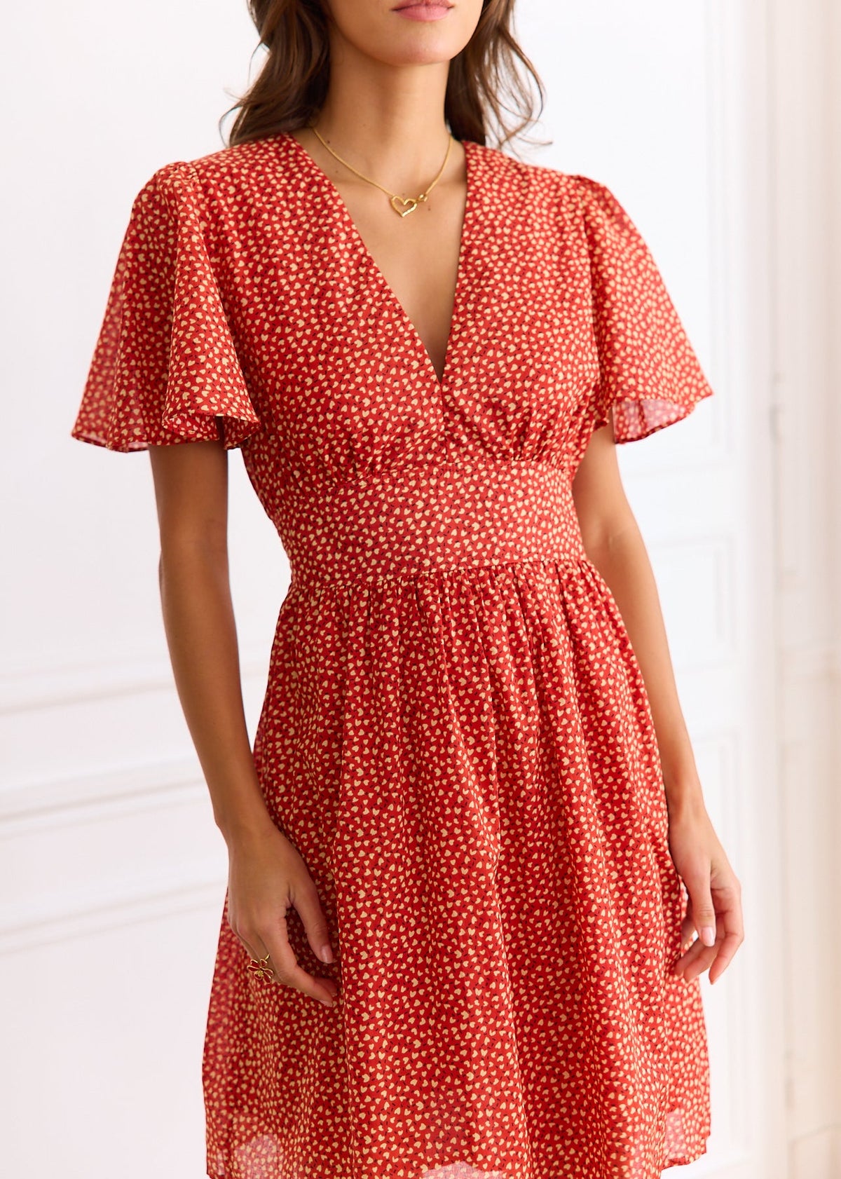 Robe courte rouge à petits motifs clairs, manches courtes et décolleté en V, portée de face.
