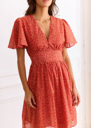 Robe courte rouge à petits motifs clairs, manches courtes et décolleté en V, portée de face.