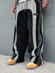 Pantalon ample à panneaux contrastants noir et gris — vue portée de trois-quarts, devant un mur gris
