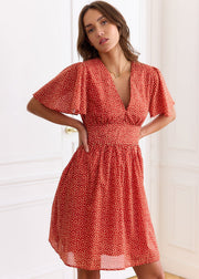 Robe rouge à petits motifs clairs, portée de face avec les mains à la taille.