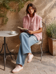 Gilet rose duveteux col montant — vue portée assise à une table de café en extérieur, livre à la main