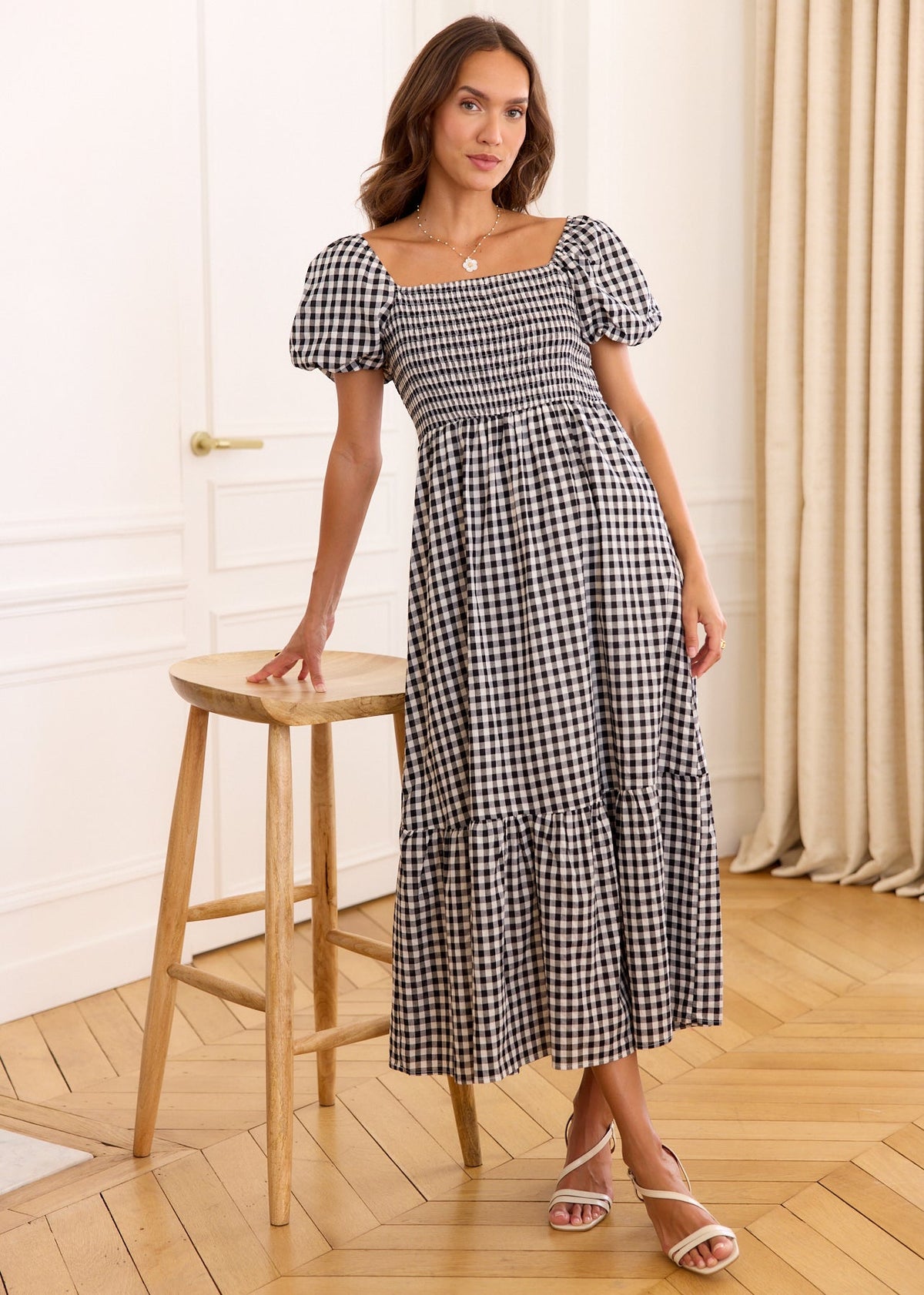 Robe longue vichy noir et blanc à buste smocké et manches bouffantes, portée près d’un tabouret.