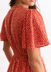Détail de la manche évasée et de l’épaule froncée au dos de la robe rouge.