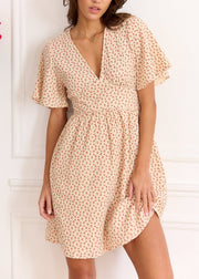 Robe beige à fleurs rouges portée de face, avec un côté de la jupe légèrement relevé à la main.