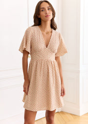 Robe beige à petites fleurs rouges, portée de face dans une pose légèrement oblique.