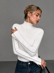 Pull col roulé passepoil contrasté blanc — vue portée de face, bras croisés, passepoil noir sur les manches