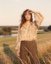 Blouse imprimée à manches ballon portée par une femme, vue de trois-quarts, main sur le front, pantalon marron