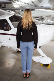Blazer cintré à épaulettes noir porté par une femme, vue de dos, avion blanc, jean clair