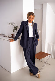 Blazer doublé à épaulettes bleu porté par une femme, vue de face, bureau blanc, tabouret