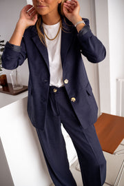 Blazer doublé à épaulettes bleu porté par une femme, vue rapprochée, pantalon assorti, main dans les cheveux
