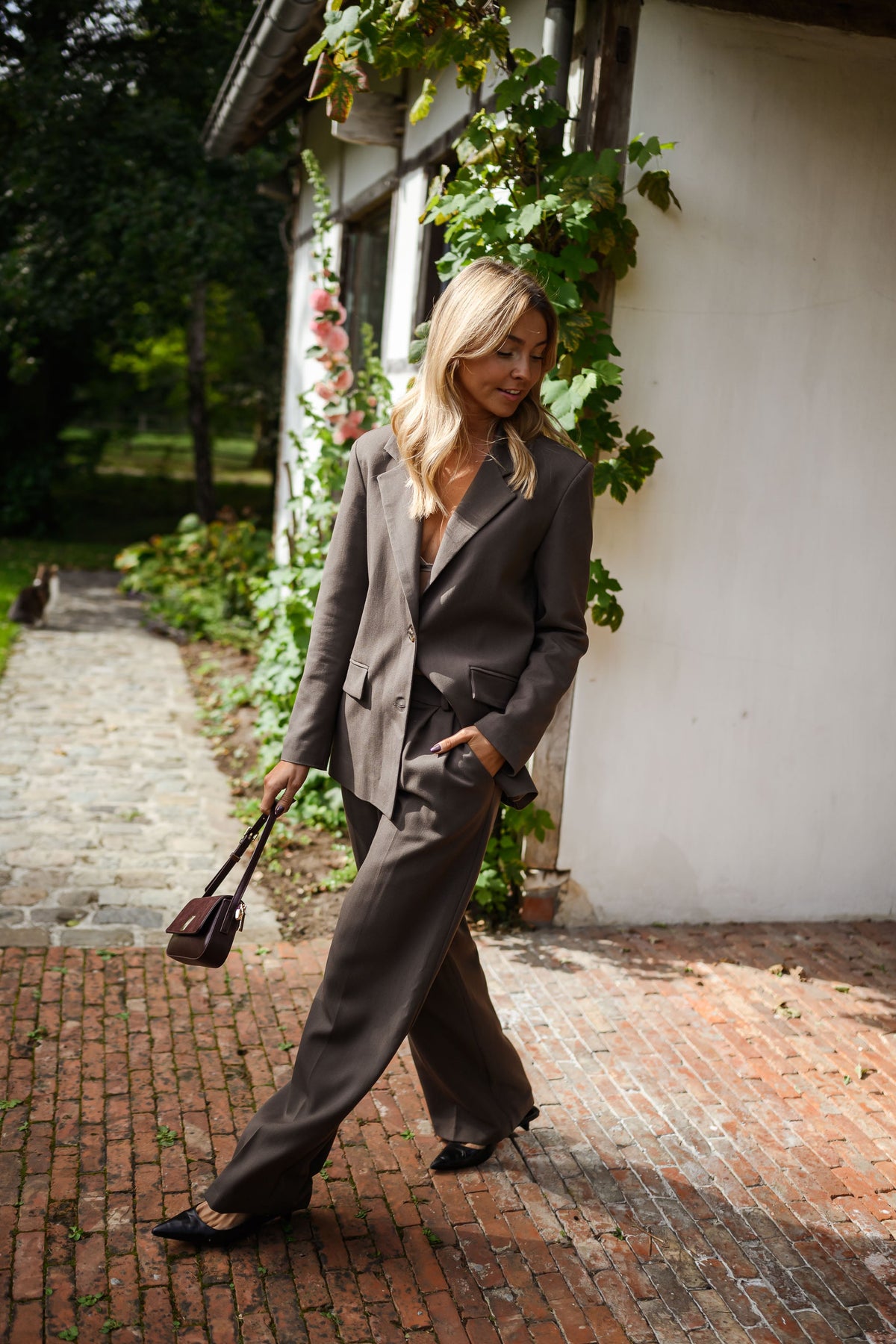 Blazer doublé à épaulettes taupe porté par une femme, vue de face, allée en briques, sac noir