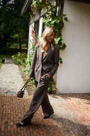 Blazer doublé à épaulettes taupe porté par une femme, vue de face, allée en briques, sac noir