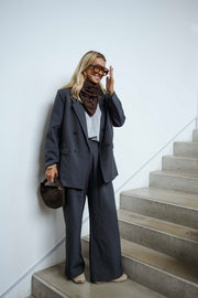 Blazer doublé à épaulettes gris porté par une femme, vue de trois-quarts, mur blanc, foulard marron