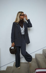 Blazer doublé à épaulettes gris porté par une femme, vue de trois-quarts, escalier, lunettes de soleil