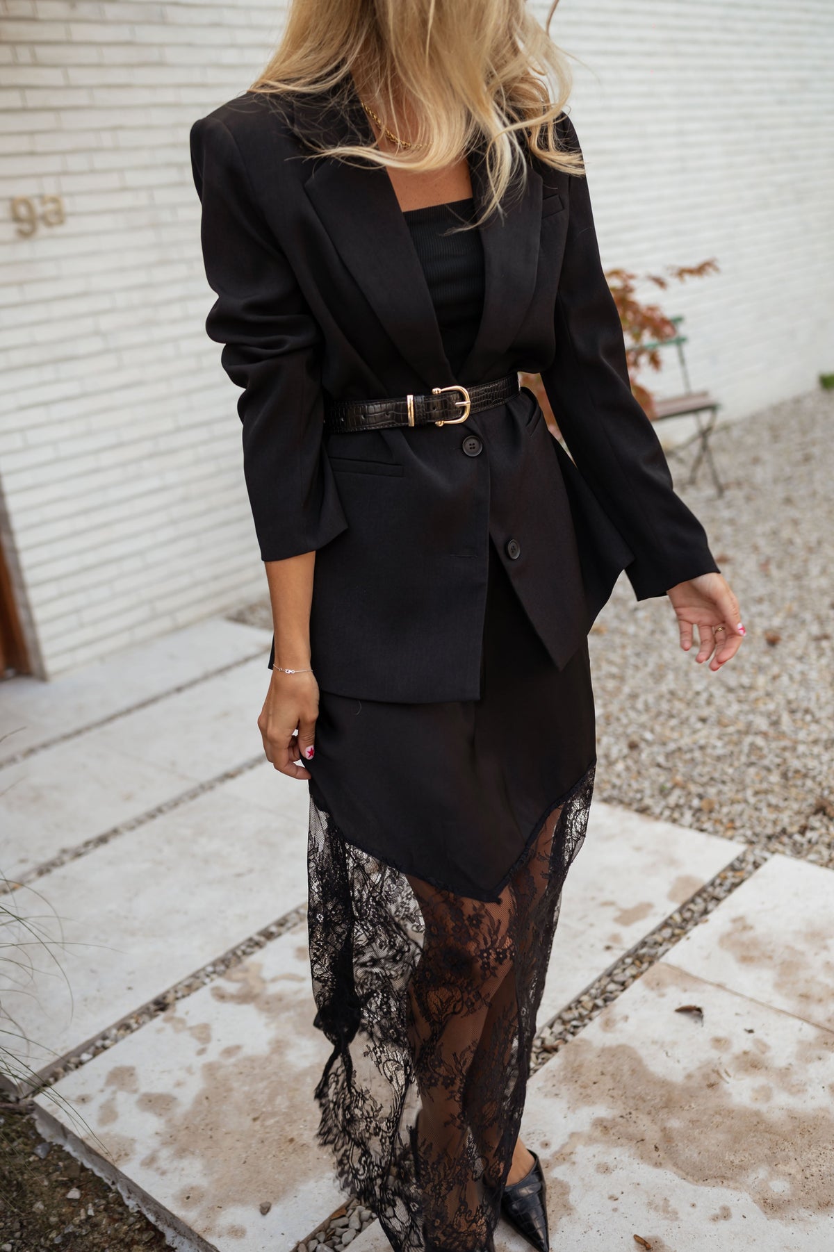 Blazer doublé à épaulettes noir porté par une femme, vue de face, jupe en dentelle, ceinture