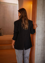 Blazer doublé à épaulettes noir porté par une femme, vue de dos, cheveux longs, porte