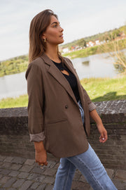 Blazer ample doublé à épaulettes chocolat porté par une femme, vue de profil, bord d'eau, jean