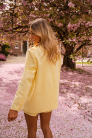 Blazer doublé à épaulettes jaune porté par une femme, vue de dos, cerisiers en fleurs