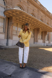 Blazer rayé cintré à épaulettes porté par une femme, silhouette entière, pantalon blanc, sac noir, devant un bâtiment