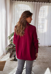 Blazer droit doublé à épaulettes bordeaux porté par une femme, vue de dos, rideaux, jean