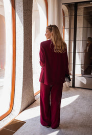 Blazer droit doublé à épaulettes bordeaux porté par une femme, vue de dos, pantalon bordeaux, baie vitrée