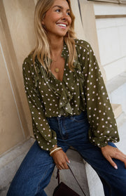 Blouse à pois col V portée par une femme, vue de trois-quarts, sourire, jean bleu