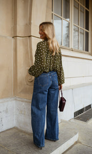 Blouse à pois col V portée par une femme, vue de dos, cheveux blonds, sac bordeaux
