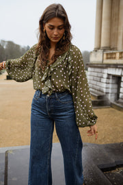 Blouse à pois col V portée par une femme, vue de face, esplanade, mains dans les poches