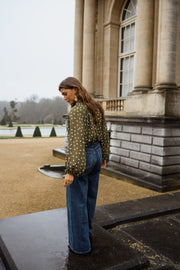 Blouse à pois col V portée par une femme, vue de dos, colonne, regard par-dessus l'épaule
