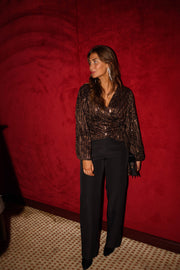 Blouse cache-cœur à sequins portée par une femme, vue de face, rideau rouge, pantalon noir