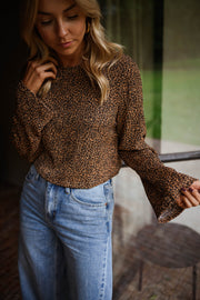 Blouse léopard à manches évasées portée par une femme, vue rapprochée, fond de verdure, main dans les cheveux
