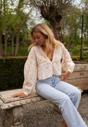 Blouse fleurie à décolleté dentelle portée par une femme, assise, banc en pierre, sourire