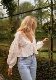 Blouse fleurie à décolleté dentelle portée par une femme, vue de trois-quarts, jardin, pergola