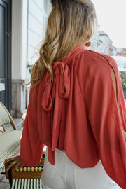 Blouse froncée à col montant terracotta portée par une femme, vue rapprochée, nœud dans le dos